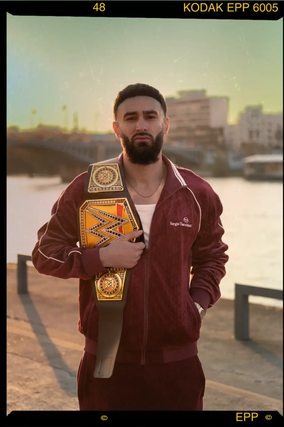 Homme en survêtement bordeaux tenant une ceinture de champion, quais de Seine